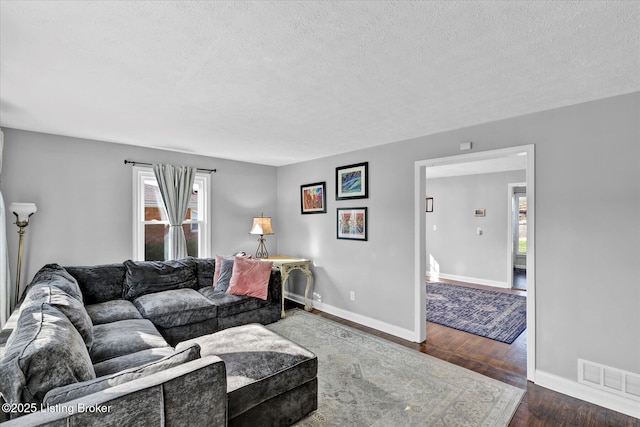 living room featuring visible vents, baseboards, a textured ceiling, and wood finished floors