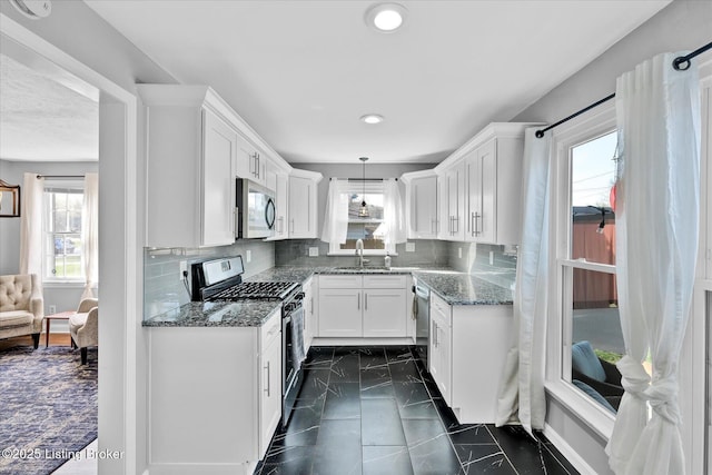 kitchen featuring a sink, appliances with stainless steel finishes, dark stone counters, and white cabinetry