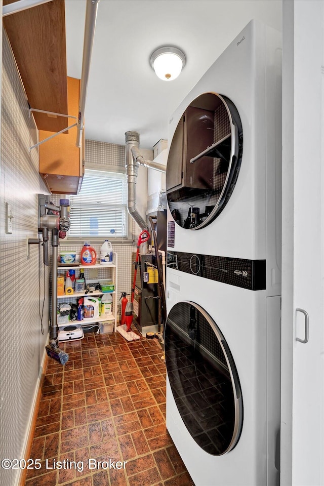 laundry room featuring stacked washing maching and dryer, baseboards, laundry area, and brick patterned floor