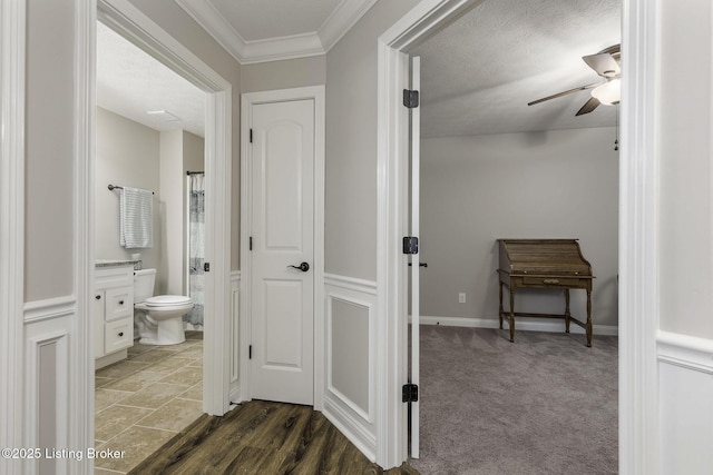corridor featuring baseboards, crown molding, dark colored carpet, and a textured ceiling