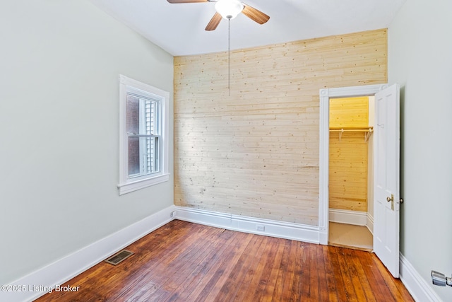 spare room featuring visible vents, baseboards, a ceiling fan, hardwood / wood-style flooring, and wood walls