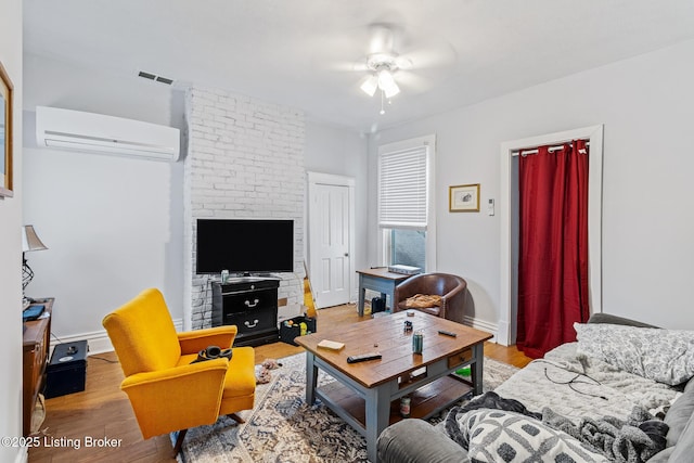 living room with visible vents, baseboards, ceiling fan, a wall mounted AC, and wood finished floors