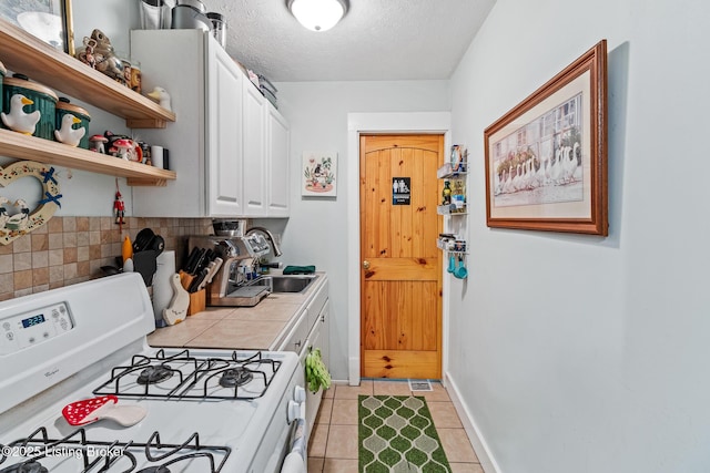 kitchen featuring light tile patterned floors, a sink, white range with gas cooktop, white cabinetry, and tile countertops