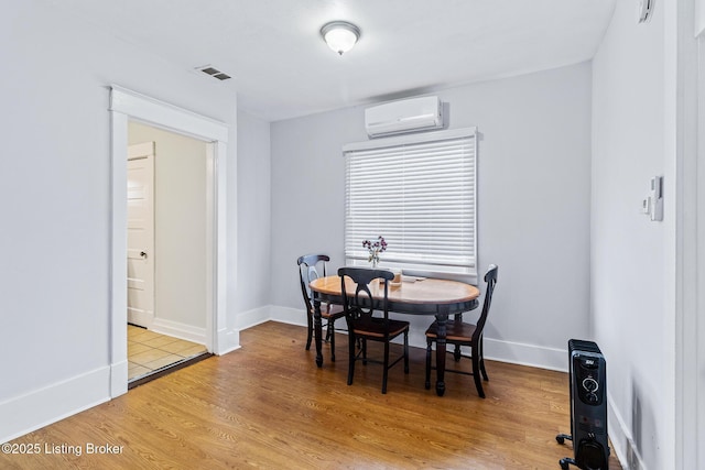 dining room featuring an AC wall unit, baseboards, light wood-type flooring, and visible vents