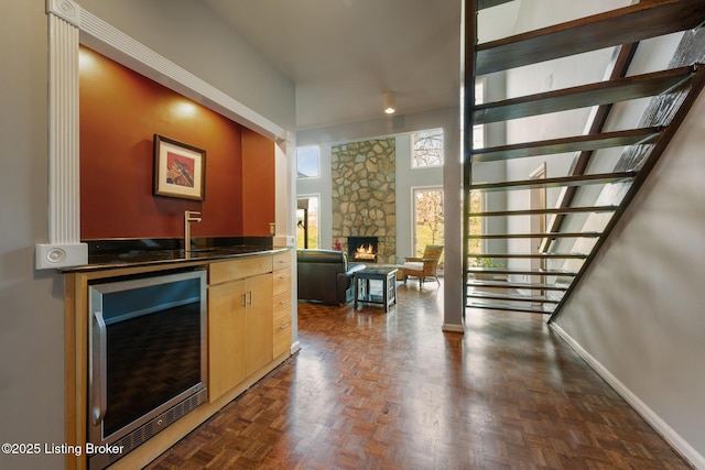 bar with bar area, a stone fireplace, baseboards, stairs, and wine cooler
