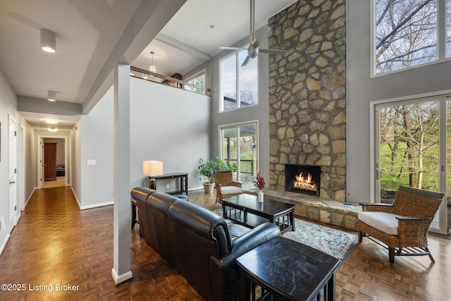 living area with baseboards, a ceiling fan, a towering ceiling, and a fireplace