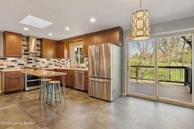 kitchen with brown cabinetry, a skylight, stainless steel appliances, decorative backsplash, and ventilation hood