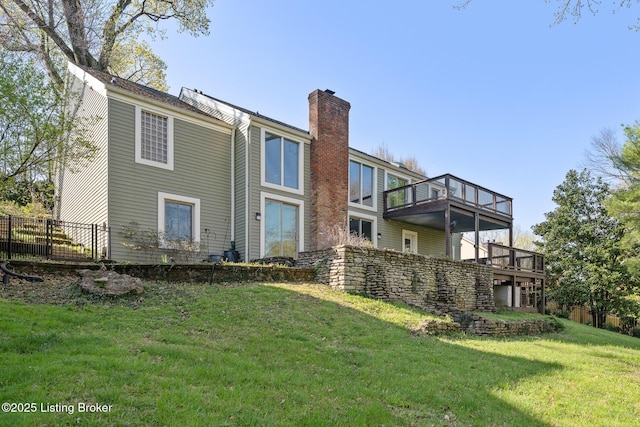 back of house with a chimney, a balcony, fence, and a lawn