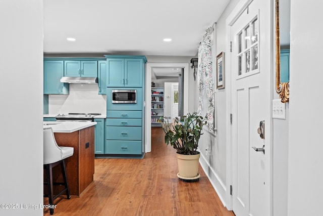 kitchen with light countertops, light wood-style floors, under cabinet range hood, stainless steel appliances, and blue cabinetry