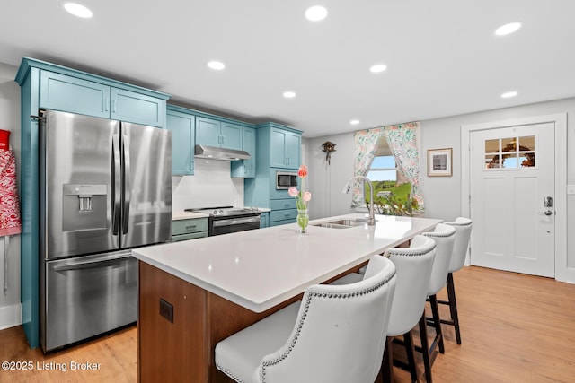 kitchen featuring blue cabinetry, under cabinet range hood, a kitchen bar, stainless steel appliances, and a sink