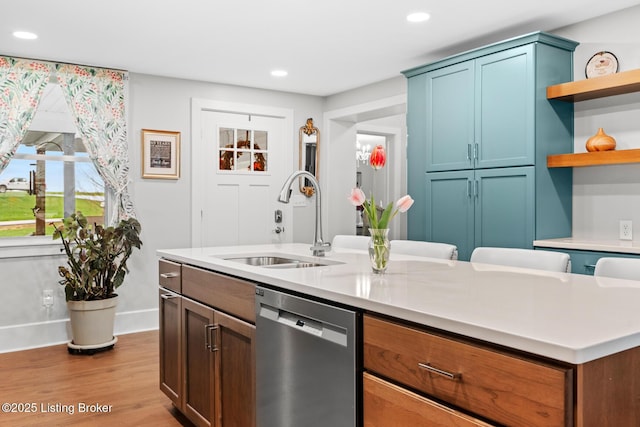 kitchen with light countertops, open shelves, stainless steel dishwasher, a sink, and wood finished floors