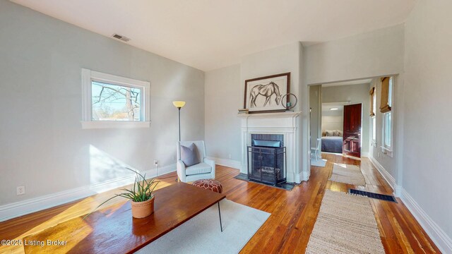 living area with visible vents, baseboards, wood finished floors, and a fireplace with flush hearth