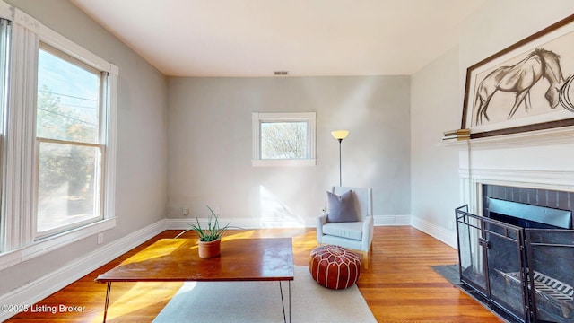 living area featuring a fireplace with flush hearth, wood finished floors, baseboards, and visible vents