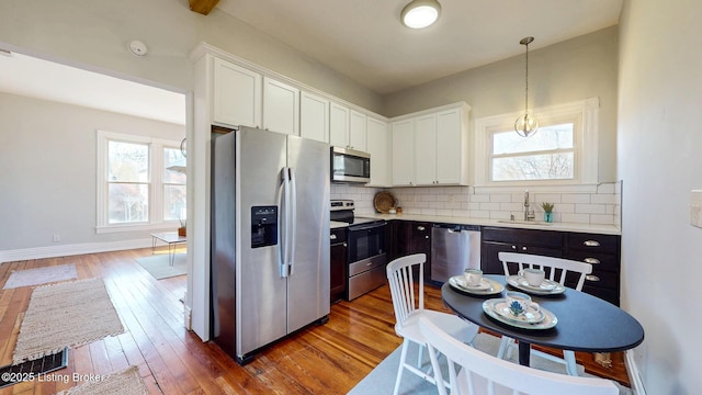 kitchen with a sink, white cabinetry, wood finished floors, stainless steel appliances, and backsplash