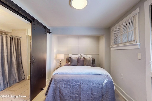 bedroom with baseboards, a barn door, and wood finished floors