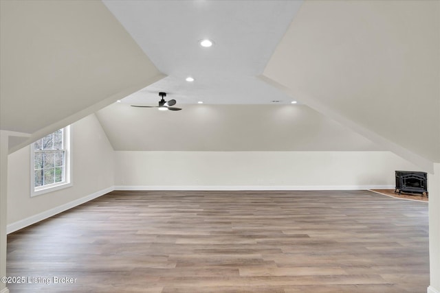bonus room with vaulted ceiling, wood finished floors, a wood stove, baseboards, and recessed lighting