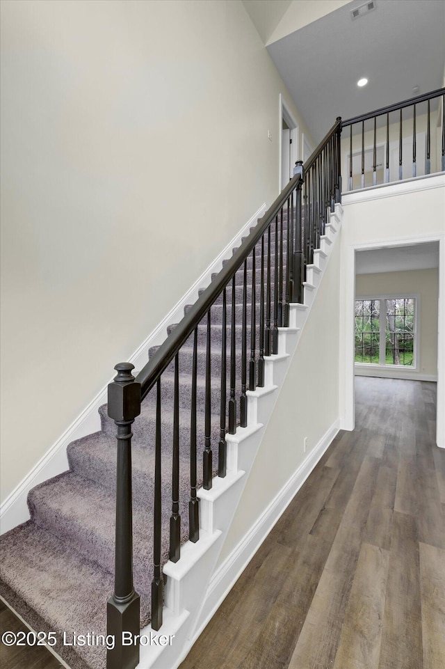 staircase with baseboards, wood finished floors, and a high ceiling