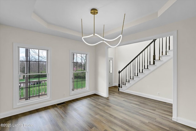 unfurnished dining area featuring a raised ceiling, wood finished floors, stairs, and baseboards