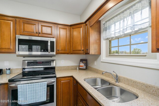 kitchen with light stone countertops, stainless steel appliances, a sink, and brown cabinetry