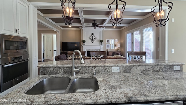 kitchen featuring appliances with stainless steel finishes, a large fireplace, light stone countertops, coffered ceiling, and a sink