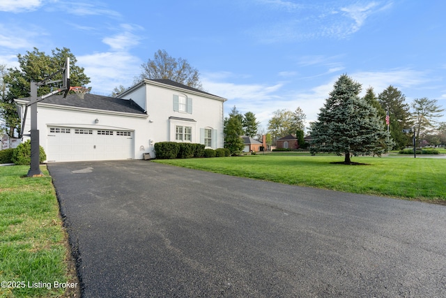 traditional-style house with a front yard, an attached garage, a chimney, aphalt driveway, and stucco siding