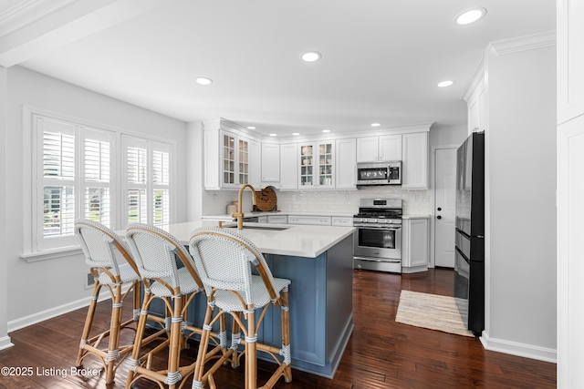 kitchen with appliances with stainless steel finishes, light countertops, a sink, baseboards, and backsplash