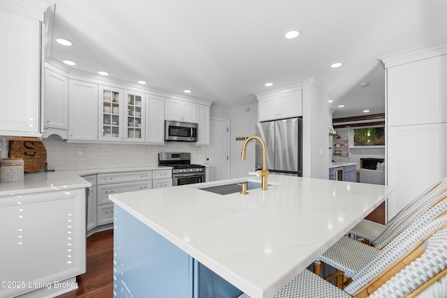 kitchen with glass insert cabinets, a sink, appliances with stainless steel finishes, white cabinetry, and backsplash