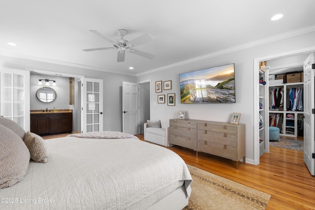 bedroom featuring wood finished floors, ornamental molding, a walk in closet, and recessed lighting