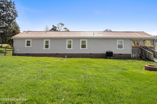 rear view of property featuring a lawn, crawl space, cooling unit, and an outdoor fire pit