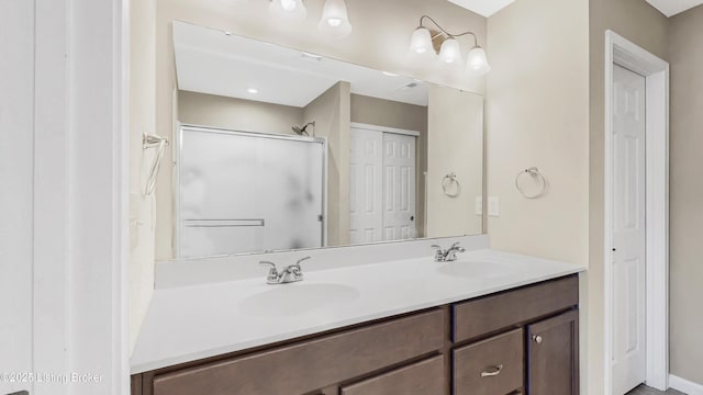 full bathroom featuring a shower with shower door, a sink, double vanity, and a closet