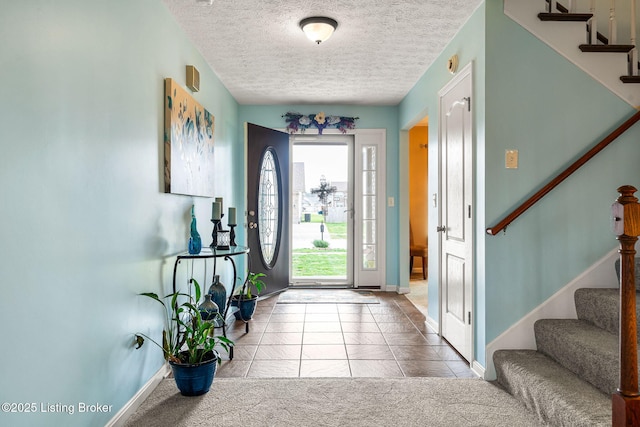 entrance foyer featuring baseboards, tile patterned flooring, stairway, a textured ceiling, and carpet floors