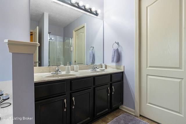 bathroom with double vanity, a textured ceiling, a shower stall, visible vents, and a sink