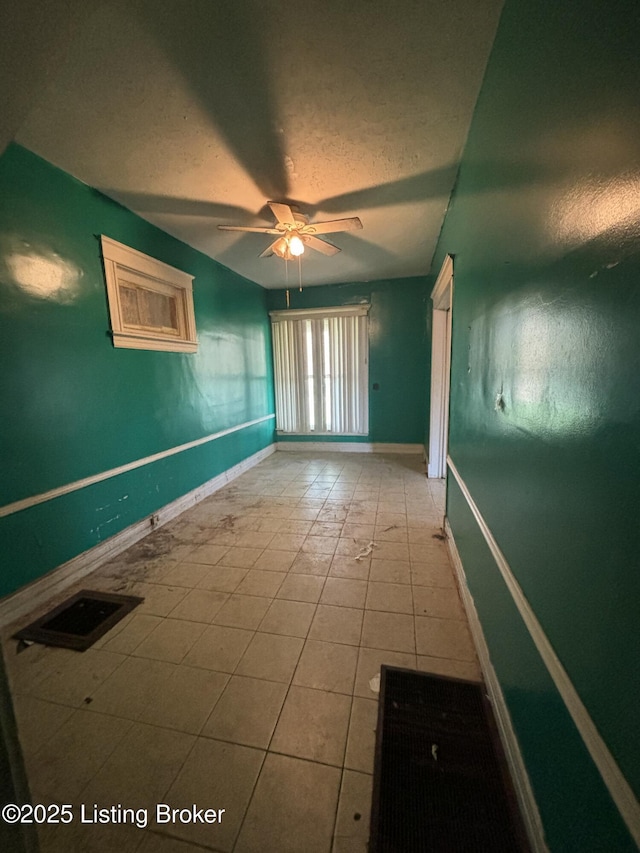empty room with tile patterned floors, a ceiling fan, baseboards, and a textured ceiling