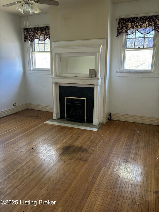 unfurnished living room featuring a wealth of natural light, a ceiling fan, hardwood / wood-style flooring, and baseboards