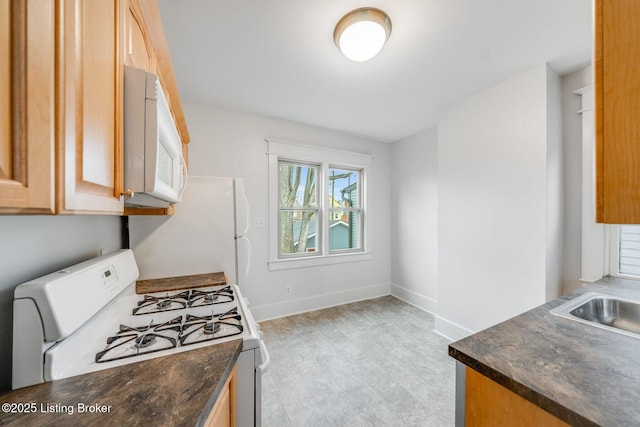 kitchen with baseboards, dark countertops, white appliances, and light floors