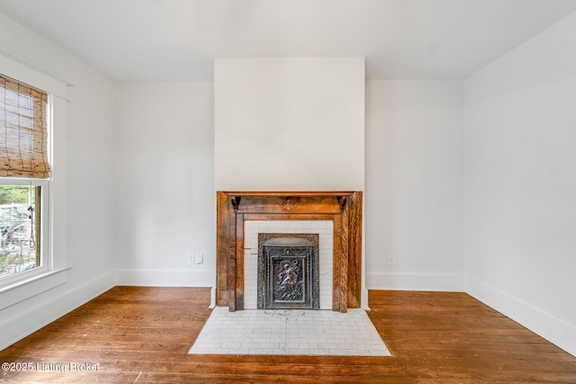 unfurnished living room featuring a brick fireplace, baseboards, and wood finished floors