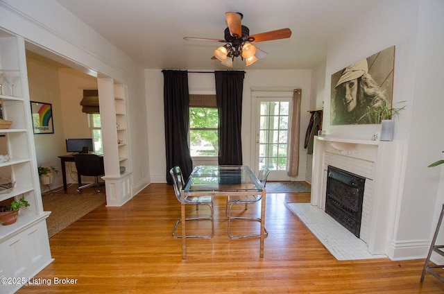 dining area featuring a tiled fireplace, light wood-style flooring, built in features, and ceiling fan