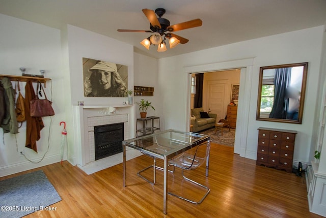 dining area featuring a fireplace with flush hearth, wood finished floors, and a ceiling fan