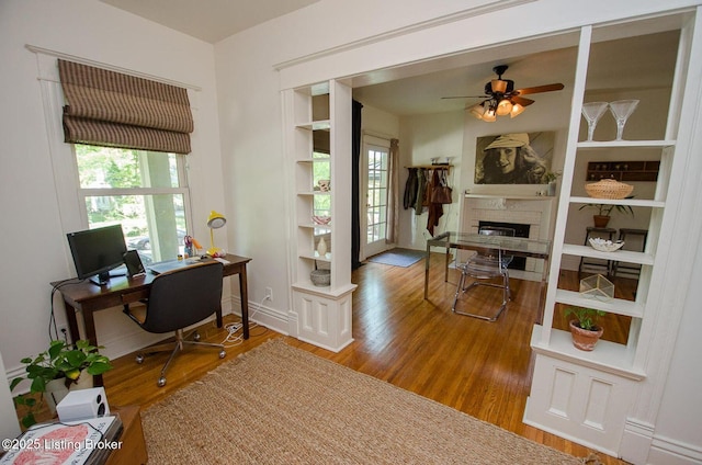 office space with a fireplace, a ceiling fan, and wood finished floors