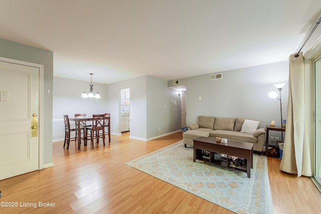 living area with light wood-style floors, baseboards, a notable chandelier, and visible vents