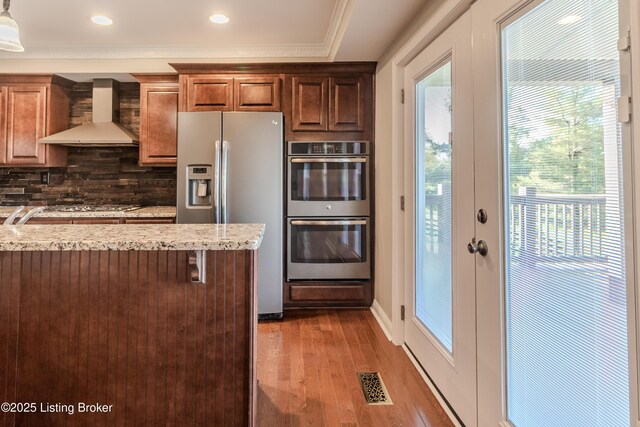 1110 Clark Station Rd, Fisherville, KY 40023 - kitchen featuring wall chimney range hood, light wood-style flooring, visible vents, decorative backsplash, and appliances with stainless steel finishes