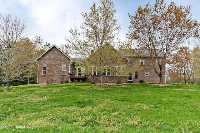 rear view of house with a lawn, a wooden deck, and brick siding