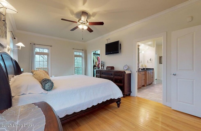 bedroom featuring a ceiling fan, crown molding, a spacious closet, light wood finished floors, and ensuite bath