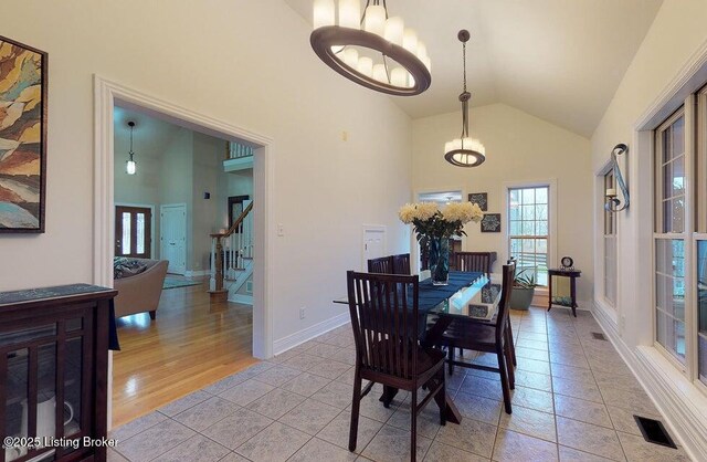dining room featuring high vaulted ceiling, stairs, light tile patterned floors, an inviting chandelier, and visible vents