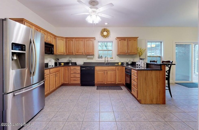 kitchen featuring a peninsula, a sink, black appliances, ceiling fan, and a breakfast bar area
