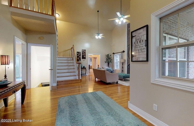 interior space with stairway, a towering ceiling, wood finished floors, a ceiling fan, and baseboards