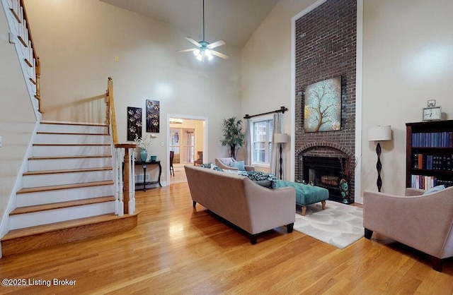 living room with stairs, a ceiling fan, high vaulted ceiling, and light wood-style floors