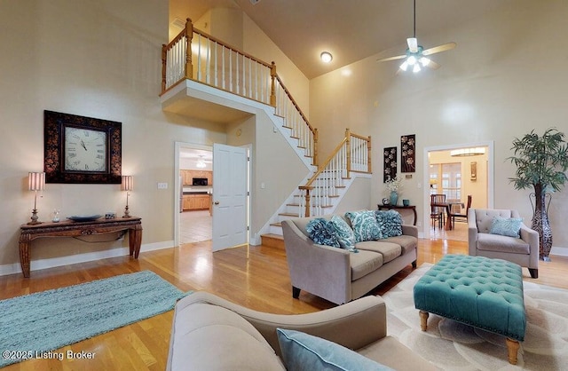 living area featuring stairway, wood finished floors, a ceiling fan, baseboards, and high vaulted ceiling