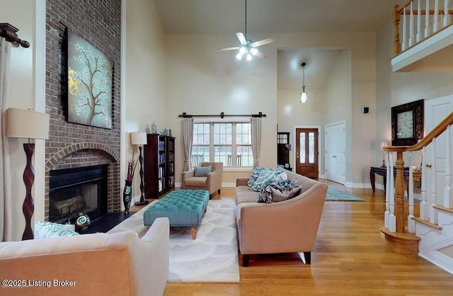 living room featuring a high ceiling, wood finished floors, a fireplace, stairs, and ceiling fan