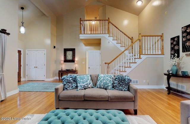 living room featuring high vaulted ceiling, stairway, wood finished floors, baseboards, and visible vents